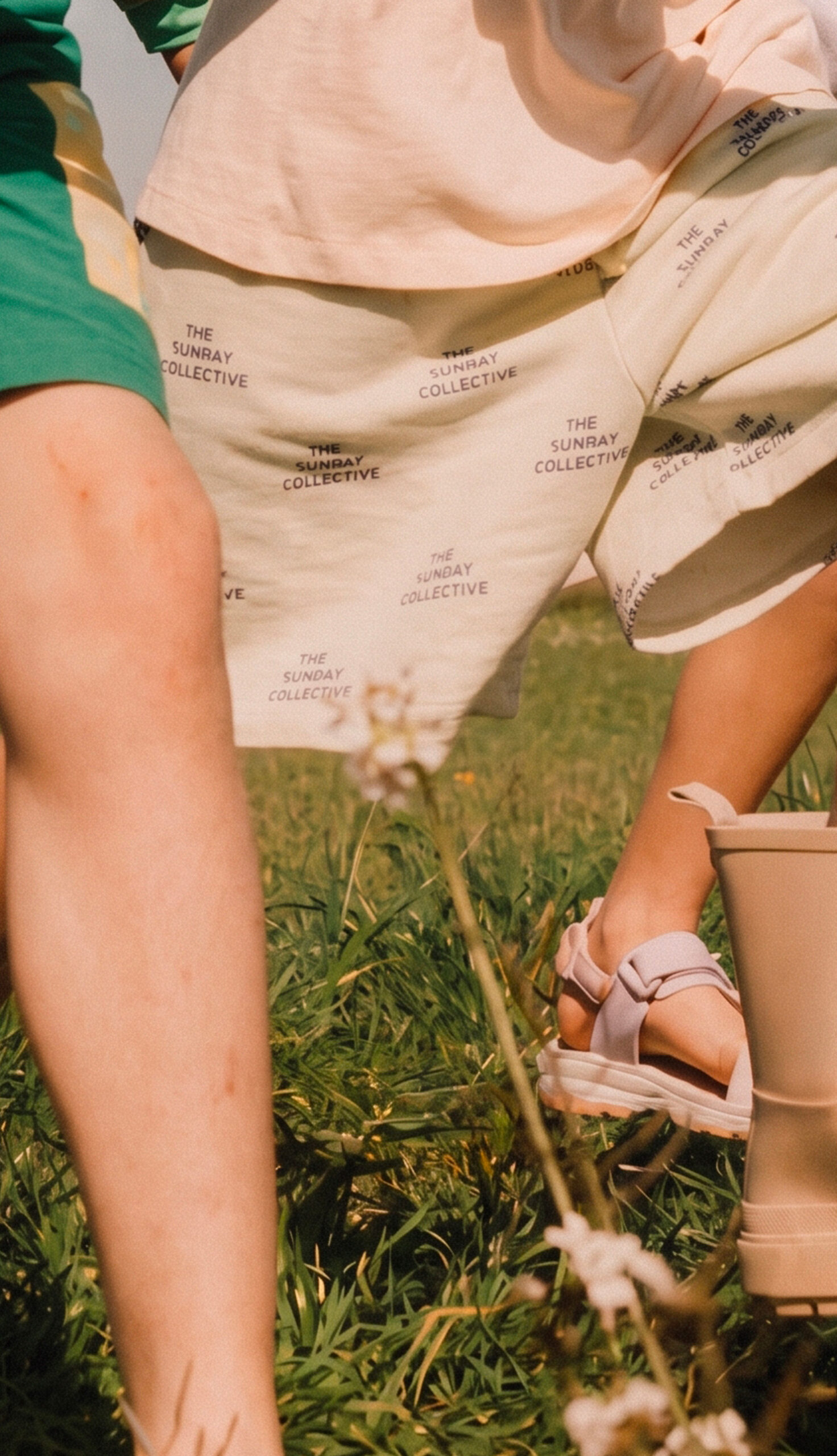 Children run barefoot through a wildflower meadow in summer, wearing casual clothing, with rolling hills visible in the background.