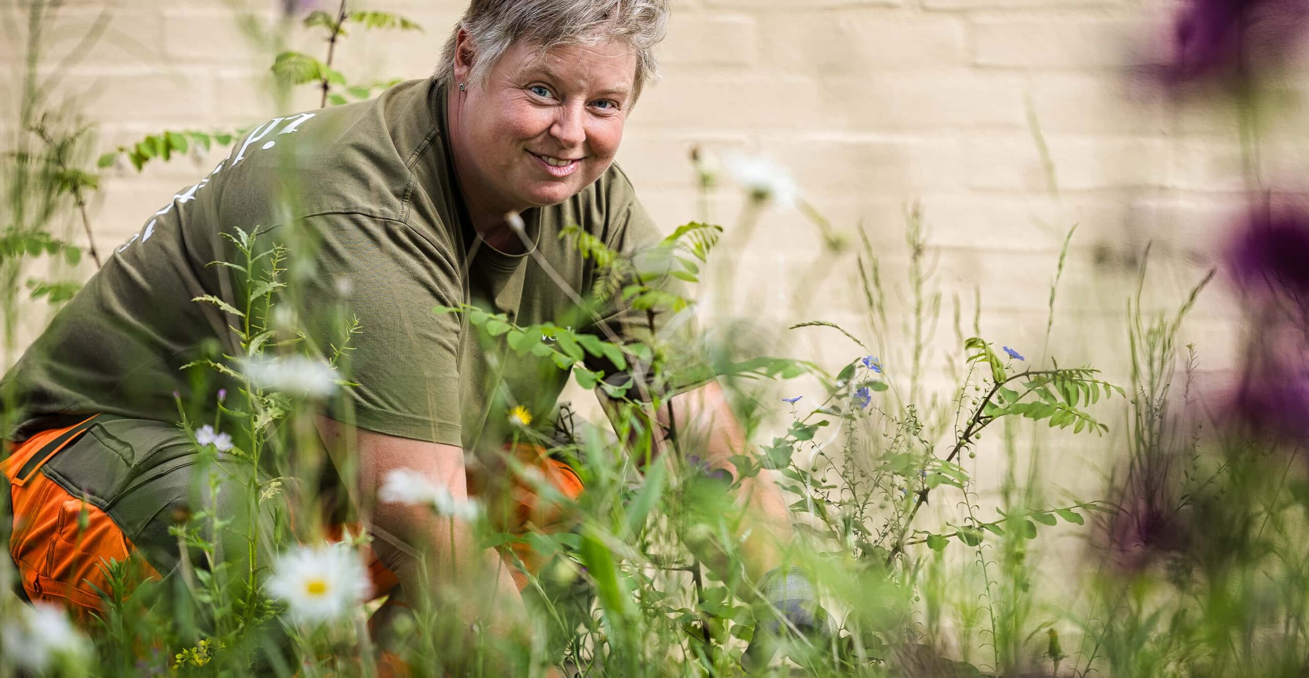 idverde team member in green uniform tending to a wildflower garden bed, smiling at camera