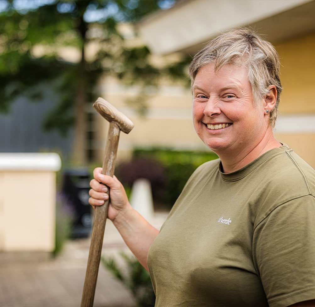 idverde employee smiling outdoors holding a wooden mallet, wearing a green branded t-shirt