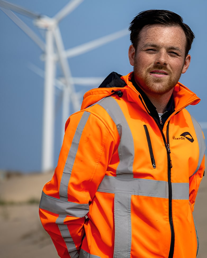 idverde worker in orange hi-vis jacket standing in front of wind turbines on a sunny day