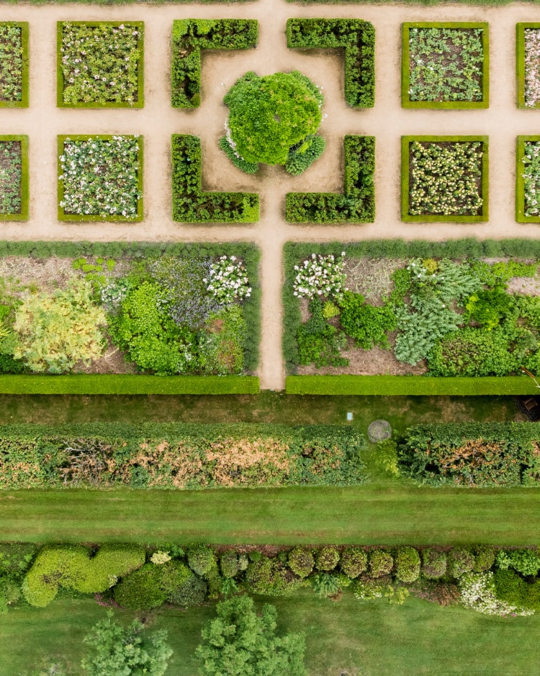 Aerial view of a formal garden with symmetrical hedged beds, gravel paths, and a central topiary feature.