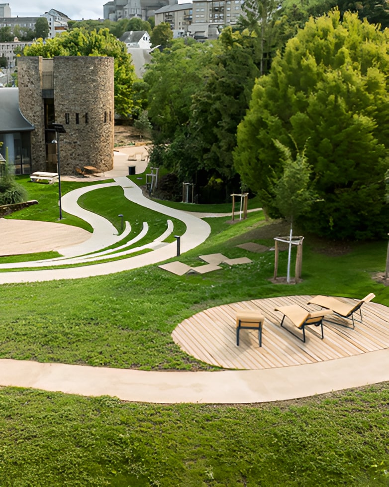 Curved pathways and circular wooden decking areas with lounge chairs in a landscaped park beside historic stone tower